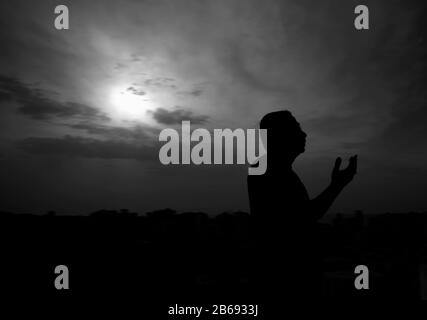 Silhouette d'un mana priant avant d'avoir son premier repas au Ramadan au coucher du soleil Banque D'Images