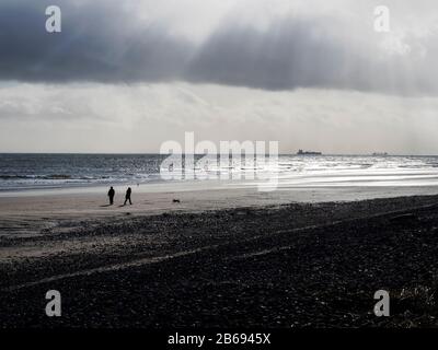 Les gens ont silhouetté contre un ciel d'hiver marchant sur la plage de Leven à Fife, en Écosse Banque D'Images