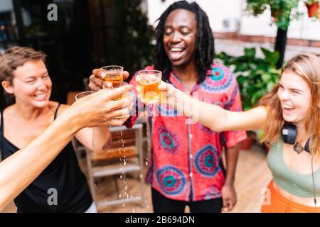 Accent sélectif sur les verres d'un groupe de quatre jeunes de différents groupes ethniques toaster avec la bière sur une terrasse avec des plantes Banque D'Images
