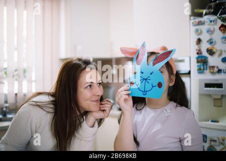 Bonne mère regardant son enfant avec un lapin sur son visage. Mère souriante regardant sa fille qui tient le lapin en papier couté sur son visage dedans Banque D'Images
