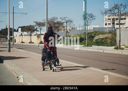 Essaouira, MAROC - 17 JANVIER 2020: Les femmes avec un poussin sur la route marchant dans la rue, portent de beaux vêtements arabes bleus et blancs Banque D'Images