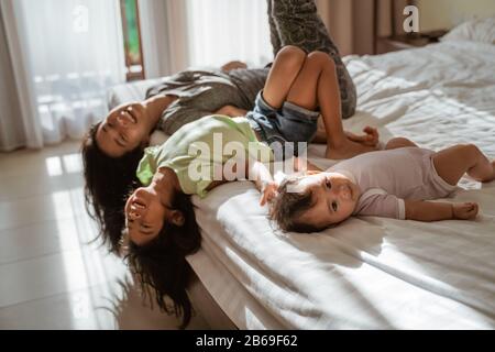 Les petits enfants asiatiques allongé dans le lit avec leur mère à côté d'eux dans la chambre à coucher Banque D'Images