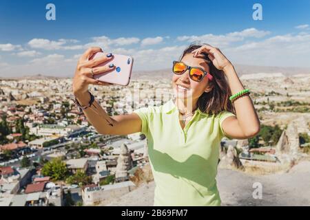 Heureuse jeune femme prenant selfie avec son smartphone avec le paysage de Cappadoce à l'arrière-plan, Göreme, Turquie Banque D'Images