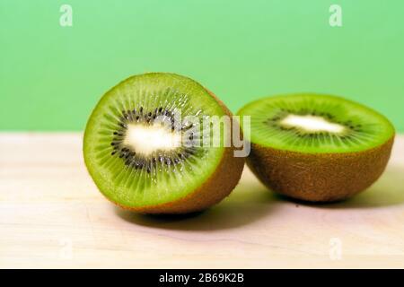 deux demi-kiwi colorés sur fond de bois et vert Banque D'Images