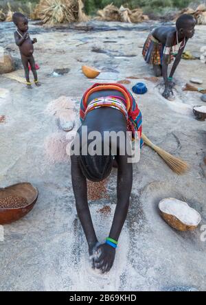 Les femmes de la tribu Larim meulant des grains de sorgho dans des trous dans un rocher, les monts Boya, Imatong, Soudan du Sud Banque D'Images