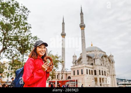 Jeune femme mangeant le bagel turc à Istanbul, Turquie sur le fond de la mosquée Ortakoy Banque D'Images