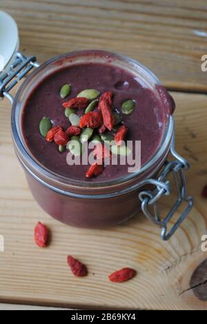 Petit bol en verre avec couvercle, rempli de smoothie végétalienne debout sur une table en bois. Le smoothie a une garniture de graines de citrouille et de baies de goji Banque D'Images