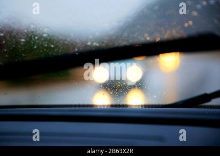 Conduite sur route sous forte pluie, essuie-glaces allumés, faible visibilité avec phares éblouissants de la circulation. Banque D'Images