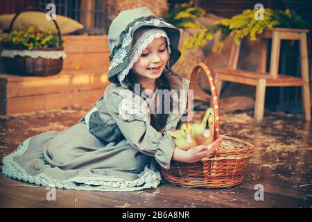 Belle fille en robe rétro avec un panier de fleurs sur un fond de paille. Style rétro. Carte de Pâques. Banque D'Images