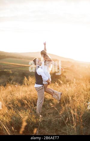 Photo de la jeune femme boho hippie portée par son beau petit ami dans le domaine de l'été. Couple s'amuser pendant leur soirée d'été à l'extérieur Banque D'Images