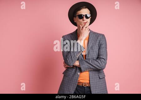 Portrait d'un jeune homme pensif séduisant portant une veste et un chapeau isolés sur fond rose Banque D'Images