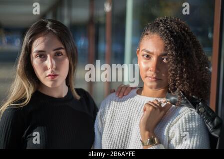 Portrait à la mode d'une paire de belles filles hispaniques debout sur fond d'un magasin. L'un d'eux tient une veste en cuir au-dessus de son moul Banque D'Images