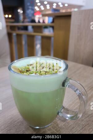 Café au Latte de pistache dans une tasse en verre avec mousse et noix sur la table dans le café. Banque D'Images