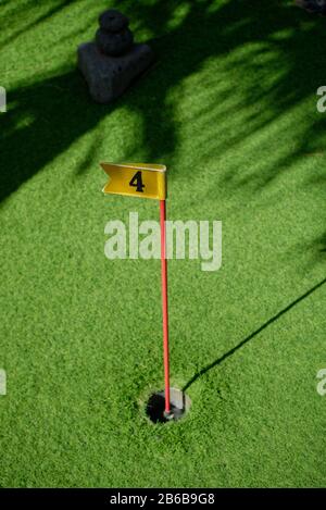 Un trou de golf à poinçonner avec un vert astrogazon et une lumière aux applis. Avec drapeau et numéro quatre sur le poteau. Banque D'Images