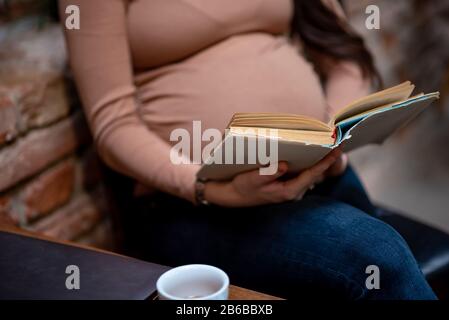 Femme enceinte lisant l'ancien livre à l'intérieur du café Banque D'Images