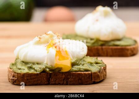 Fuite de jaune poché. Sandwichs avec œufs pochés et pâte d'avocat sur pain de céréales. Mode de vie sain. Banque D'Images