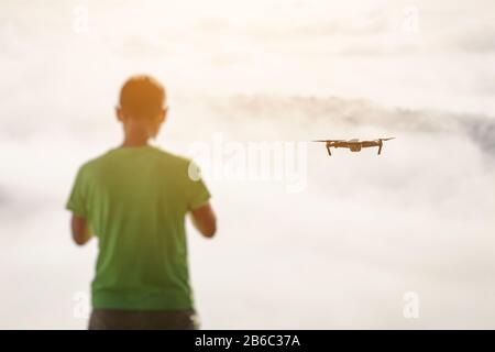 Jeune homme naviguant sur un drone volant au brouillard et aux nuages, debout au-dessus des montagnes au coucher du soleil Banque D'Images