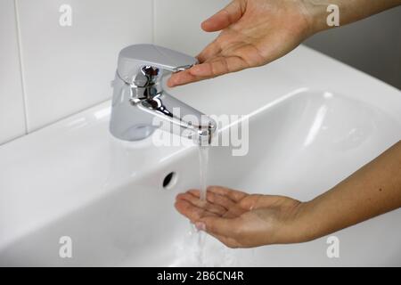 COVID-19 se laver les mains dans l'évier de salle de bains à la maison contre le coronavirus de Novel (2019-nCoV). Femme mains vérification de la température touchant l'eau courante avec ha Banque D'Images