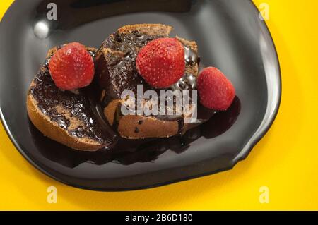 représentant deux morceaux de gâteau enrobé de chocolat avec plusieurs fraises sur le dessus en plaque noire sur fond de table jaune Banque D'Images