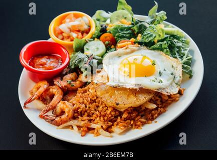 Gros plan sur une assiette blanche de riz frit à l'ananas asiatique, accompagné d'une salade d'œufs, de crevettes et de légumes frits Banque D'Images