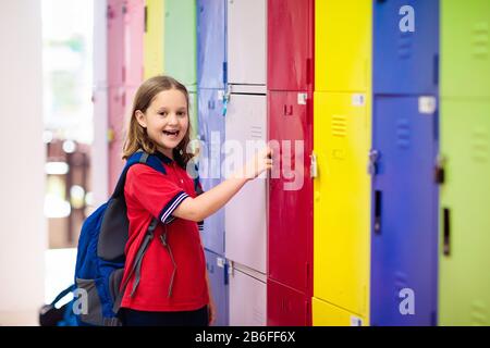 Étudiant à l'école au casier. Étude des enfants. Petite fille en uniforme tenant la clé de cadenas dans la salle préscolaire. Enfant avec sac à dos et livres. Banque D'Images