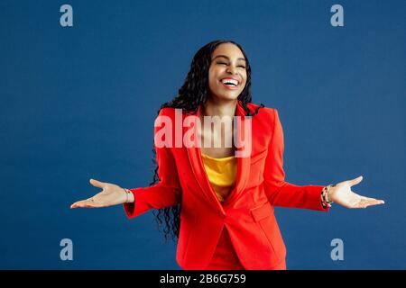 Portrait d'une jeune femme souriante très heureuse en costume rouge d'affaires avec bras dehors, isolé sur fond bleu Banque D'Images