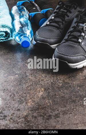 Concept de forme physique. Chaussures de sport noires, serviette, haltères et bouteille d'eau sur la vieille table. Banque D'Images