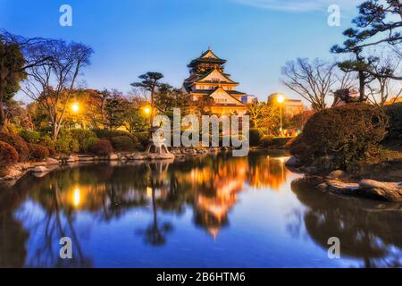 Toujours étang dans le jardin japonais traditionnel de la ville d'Osaka avec tour historique et des lumières de rue reflétant au lever du soleil. Banque D'Images