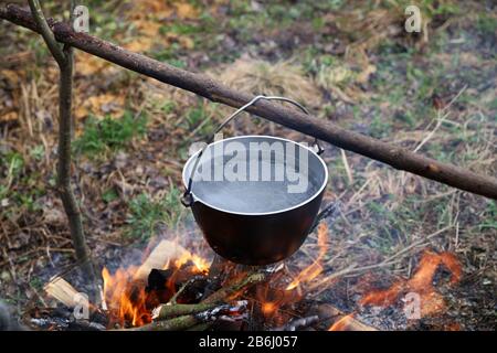 Chaudron au feu lors d'un voyage de randonnée. L'eau est bouillante dans un pot en métal sur feu de camp. Faire cuire du thé ou de la nourriture dans le camp dans la nature Banque D'Images