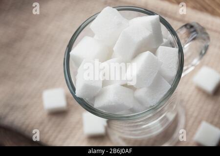 Cubes de sucre blanc dans une tasse de verre sur un fond de serviette beige. Gros plan, mise au point sélective, vue de dessus Banque D'Images