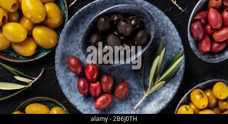 Panorama des olives en hauteur. Un assortiment d'olives vertes, noires et rouges, tirées du dessus sur une table sombre Banque D'Images