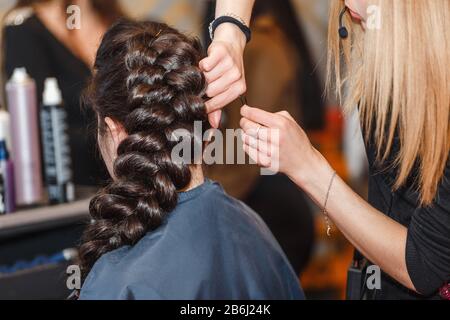 Coiffeur professionnel faisant une coiffure de beauté avec une grande tresse à la brunette cheveux Banque D'Images