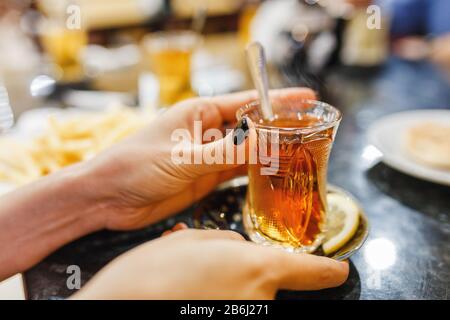 Thé turc avec verre de thé traditionnel dans un café, avec une main féminine au premier plan Banque D'Images