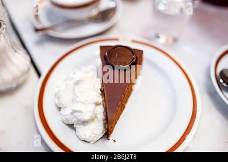 24 MARS 2017, VIENNE, AUTRICHE : le gâteau authentique de Viennese Sacher Torte servi avec de la crème fouettée et une tasse de café au Sacher Hotel Cafe Banque D'Images