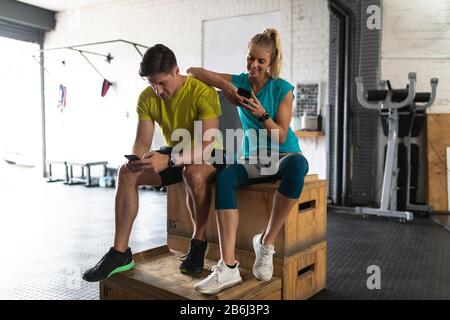 Couple sportif dans la salle de sport de cross-training à l'aide de leur téléphone Banque D'Images