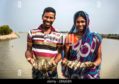 Un homme et une femme tiennent le poisson dans leur main et le visage heureux car ils sont heureux avec le poisson et les crevettes qu'ils ont récoltées de leur étang. Banque D'Images