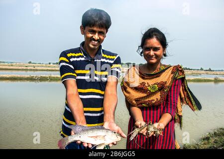 Un homme et une femme tiennent le poisson dans leur main et le visage heureux car ils sont heureux avec le poisson et les crevettes qu'ils ont récoltées de leur étang. Banque D'Images