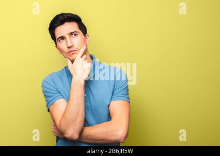 pensif beau homme en chemise bleue avec la main sur son menton regardant vers le haut contre fond jaune avec espace de copie Banque D'Images