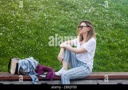 Femme assise dans le parc sur fond vert floral, concept de style de vie printanier, style moderne décontracté Banque D'Images