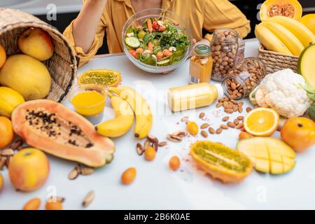 Femme mangeant une salade à la table pleine de légumes et de fruits crus sains, vue sur la culture sans visage. Concept de végétarisme, de saine alimentation et de bien-être Banque D'Images