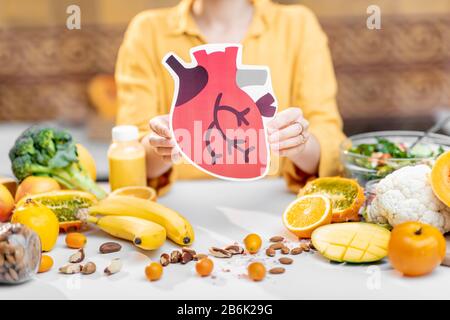 Tenir le modèle de coeur humain avec une variété de nourriture fraîche saine sur la table. Concept de nutrition équilibrée pour la santé cardiaque Banque D'Images