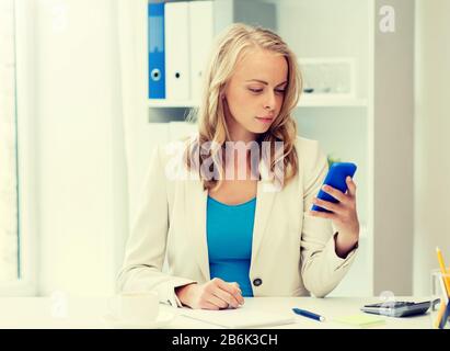 business, technology, people and communication concept - business woman texting sur smartphone au bureau Banque D'Images