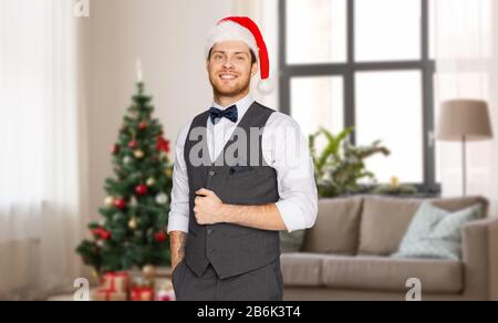 concept de célébration, de personnes et de vacances - heureux homme à santa hat et suit sur arbre de noël sur fond de maison Banque D'Images