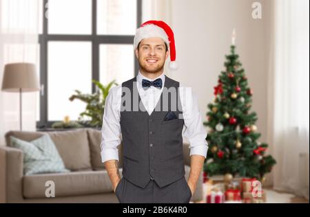 concept de célébration, de personnes et de vacances - heureux homme à santa hat et suit sur arbre de noël sur fond de maison Banque D'Images