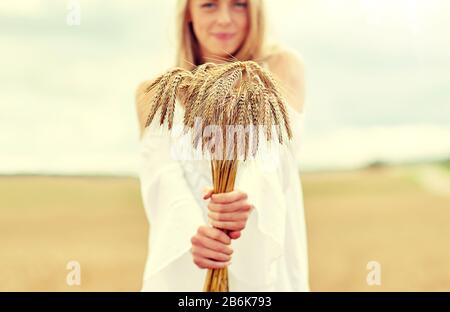 pays, nature, vacances d'été, vacances et concept de personnes - gros plan de jeune femme souriante en robe blanche avec des spikelets sur le terrain de céréales Banque D'Images