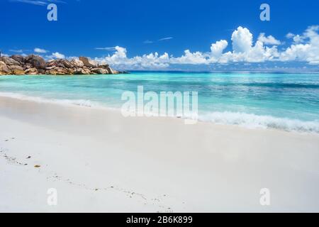 Plage de Grand Anse sur l'île de la Digue aux Seychelles. Plage de sable avec baie d'océan bleu peu profonde, nuages blancs en arrière-plan. Banque D'Images