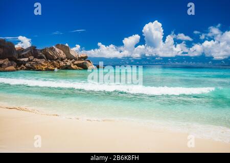 Plage de Grand Anse sur l'île de la Digue aux Seychelles. Vagues ondulantes sur la plage de sable avec lagon bleu de l'océan. Nuages blancs en arrière-plan. Banque D'Images