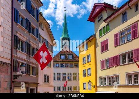 Drapeau suisse waving, église et façades colorées de maisons de la vieille ville de Zurich, la plus grande ville de Suisse en journée ensoleillée. Banque D'Images