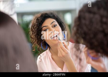 Une femme aux cheveux sombres qui met le rouge à lèvres sur ses lèvres Banque D'Images