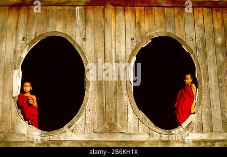 Deux moines novices encadrés par des fenêtres ovales dans le beau monastère en bois Shwe Yan Bye à Nyaung Shwe près d'Inle Lake, Myanmar. Banque D'Images